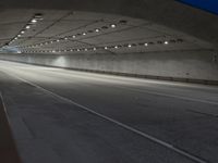 an empty highway in a tunnel with the lights on and the road lined up at the end