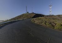 two wind towers on a hillside above an empty road and hilltop with a few rocks