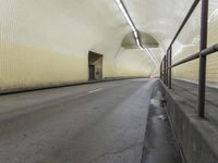 an empty roadway under a building with a white light on one corner and a tan and black wall and ceiling