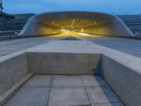 a large concrete bench and stairs in a tunnel with lights shining on the wall behind it