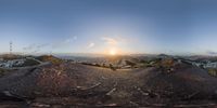 the sun setting over a city and mountains above a hill in front of the camera