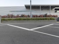 a parking lot with several empty cars in it and plants outside of the building on each side