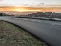 the person is riding their bicycle down the road while the sun sets over the water