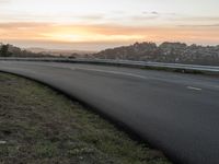 the person is riding their bicycle down the road while the sun sets over the water