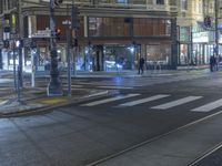 a city street at night with traffic lights on and people on the sidewalk walking past