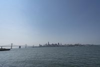 a very wide body of water with many boats floating along the bridge over it and a city in the back