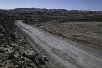 the dirt road is winding through a barren area surrounded by rocks and boulders along both sides