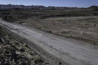 the dirt road is winding through a barren area surrounded by rocks and boulders along both sides