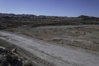 the dirt road is winding through a barren area surrounded by rocks and boulders along both sides