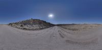 a sunny day at the end of a dirt road, with a half moon in the sky