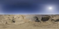 a desert area with sand and rocks near the sun and the sky is clear with a lens