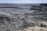 a valley of gray colored rock that resembles a desert land, with dirt, sand and some vegetation in the foreground