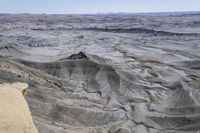 a valley of gray colored rock that resembles a desert land, with dirt, sand and some vegetation in the foreground