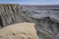 a valley of gray colored rock that resembles a desert land, with dirt, sand and some vegetation in the foreground