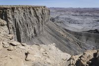 a valley of gray colored rock that resembles a desert land, with dirt, sand and some vegetation in the foreground