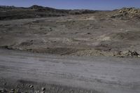 an image of desert in the distance with dirt, rocks and plants on it and a motorcycle going down it