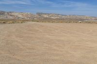 there is a field of sand with mountains in the background and a light blue sky above