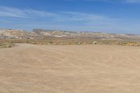 there is a field of sand with mountains in the background and a light blue sky above