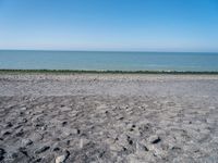 the empty beach is very deserted by the water with lots of gravel and rocks all around it