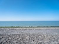 the empty beach is very deserted by the water with lots of gravel and rocks all around it