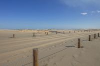 an empty road surrounded by sand dunes and fences in the desert area, with blue sky in the background