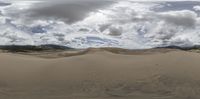 a desert with a cloudy sky and few clouds above it with some mountains in the background