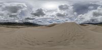 the sand has footprints in it and mountains in the background, with a cloudy sky