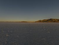 a desert in the middle of a desert plain with mountains behind it and a blue sky