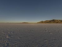 a desert in the middle of a desert plain with mountains behind it and a blue sky