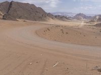 a large desert area with a long dirt road through the middle of it, surrounded by mountains