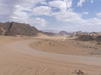 a large desert area with a long dirt road through the middle of it, surrounded by mountains