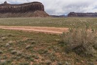 a white truck sitting in the middle of a dirt road and in the distance, an out of focus rock