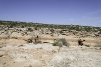 a landscape of rocks, trees, and grass with a dirt trail that winds up to the canyon