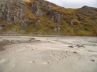 a group of people standing on top of a sandy beach near a large rocky hill