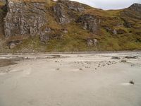 a group of people standing on top of a sandy beach near a large rocky hill