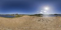 an 360 - view photograph of a sandy beach next to some water and a sunny sky