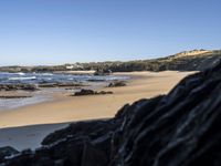 a sandy beach with blue water, rocks and cliffs in the background and waves breaking on the shore