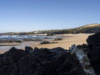 a sandy beach with blue water, rocks and cliffs in the background and waves breaking on the shore