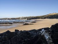 a sandy beach with blue water, rocks and cliffs in the background and waves breaking on the shore