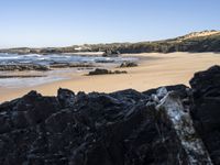 a sandy beach with blue water, rocks and cliffs in the background and waves breaking on the shore