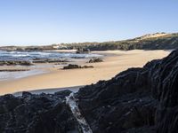 a sandy beach with blue water, rocks and cliffs in the background and waves breaking on the shore