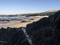 a sandy beach with blue water, rocks and cliffs in the background and waves breaking on the shore