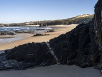 a sandy beach with blue water, rocks and cliffs in the background and waves breaking on the shore