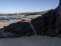 a sandy beach with blue water, rocks and cliffs in the background and waves breaking on the shore