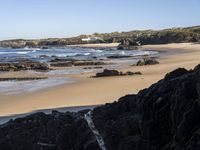 a sandy beach with blue water, rocks and cliffs in the background and waves breaking on the shore