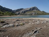 a lone motorcyclist parked on a rocky lake side near a mountain range