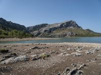 a lone motorcyclist parked on a rocky lake side near a mountain range