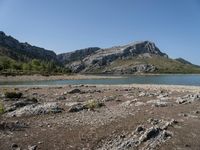 a lone motorcyclist parked on a rocky lake side near a mountain range