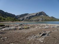 a lone motorcyclist parked on a rocky lake side near a mountain range