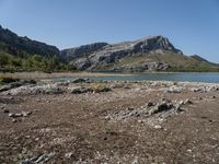 a lone motorcyclist parked on a rocky lake side near a mountain range